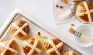 Aksamitne, błyszczące hot cross buns z rodzynkami, gotowe do pieczenia. Pędzelek i lukier czekają.
