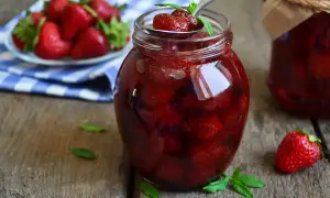 Słoik pełen słodkich, soczystych truskawek w syropie, gotowych do spożycia. Obok świeże owoce i listki mięty.
