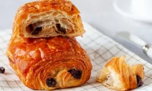 Chrupiące, złociste pain au chocolat z kawałkami czekolady, jeden przekrojony, ukazujący puszyste wnętrze.