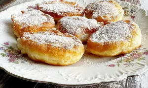 Puszyste placki z jabłkami na jogurcie, posypane cukrem pudrem, prezentują się apetycznie na ozdobnym talerzu.