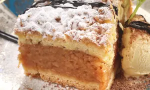Pyszna szarlotka z kruszonką, posypana cukrem pudrem, z gałką lodów waniliowych. Idealna na deser, gdy zastanawiasz się, jak zrobić jabłka do szarlotki.