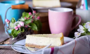 Pyszny sernik na talerzyku, obok różowy kubek i kwiaty. Zastanawiasz się, ile można przechowywać sernik w lodówce?