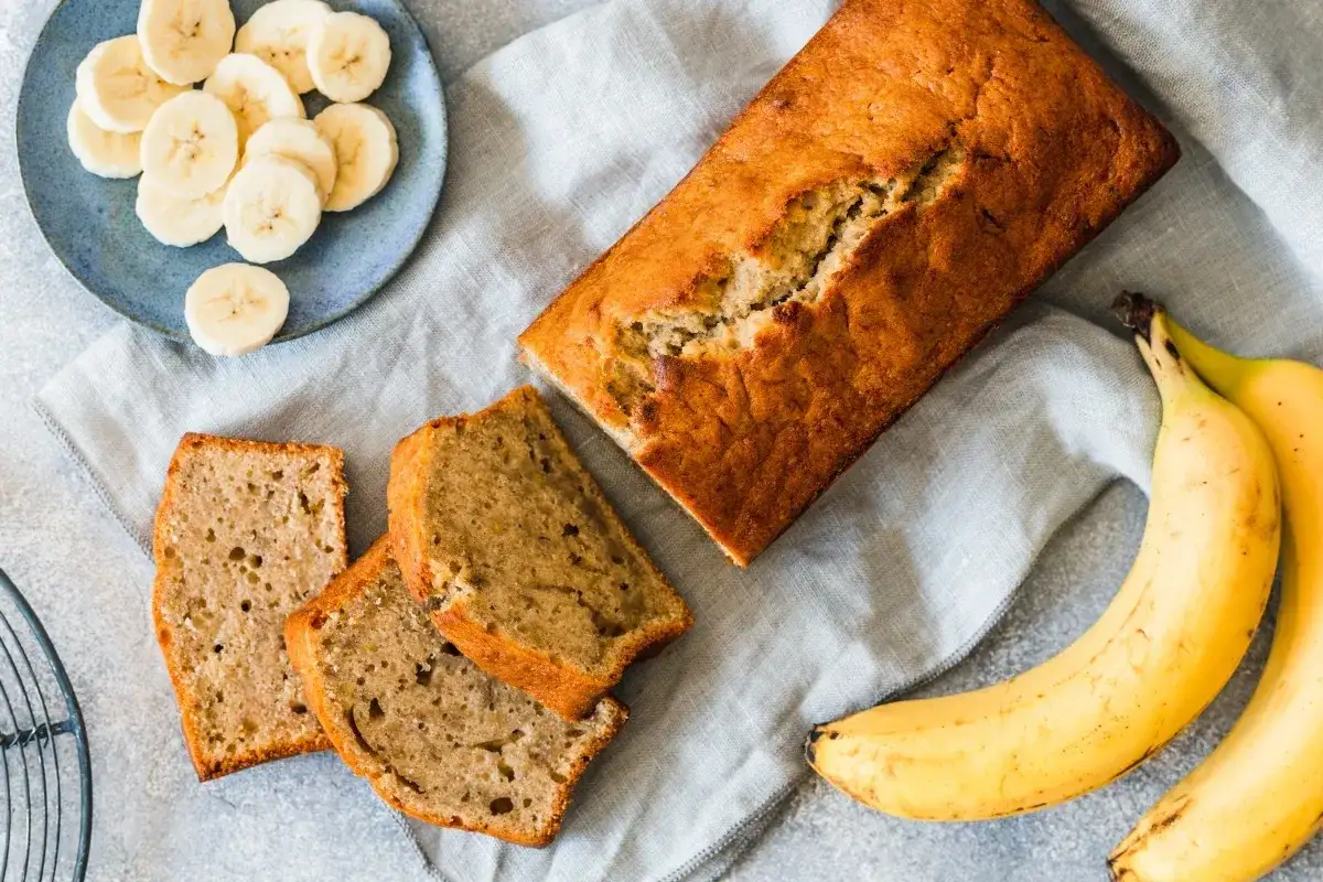 Pyszny chlebek bananowy moje wypieki, pokrojony w kromki, obok świeże banany i talerzyk z plasterkami.