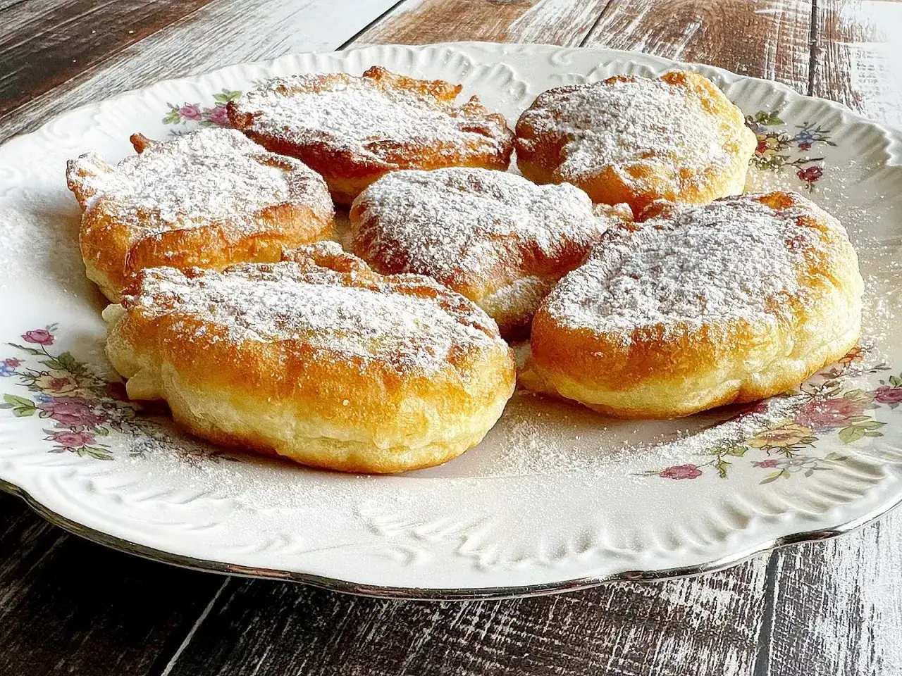 Puszyste placki z jabłkami na jogurcie, posypane cukrem pudrem, prezentują się apetycznie na ozdobnym talerzu.