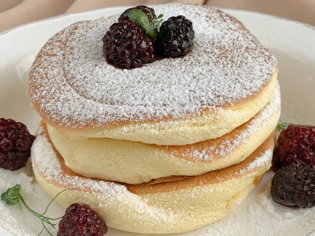 Puszyste pancakes na maślance, posypane cukrem pudrem i udekorowane jeżynami. Idealne na słodkie śniadanie.