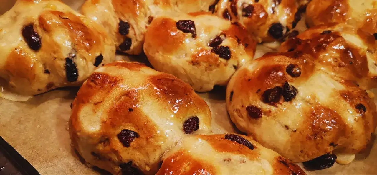 Złociste, błyszczące hot cross buns z rodzynkami, gotowe do podania.