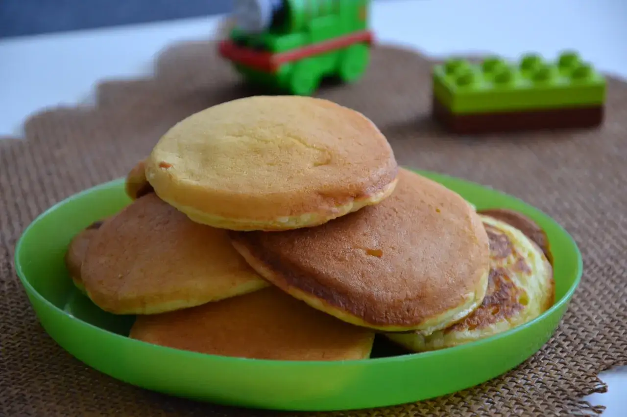 Puszyste pancakes na maślance, idealne na śniadanie. Na zielonym talerzyku, w tle zabawki.
