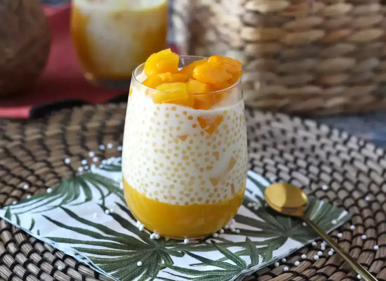 Pyszna tapioka z mango w szklance, ozdobiona owocami i podana na serwetce z motywem liści.