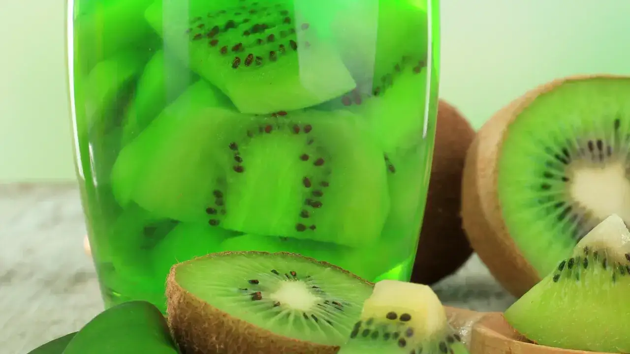 Zielona galaretka z kawałkami kiwi w szklance. Obok przekrojone kiwi. Jak zrobić, aby galaretka stężała z kiwi?