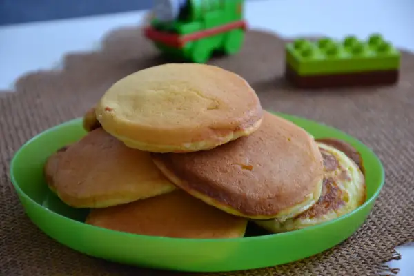 Puszyste pancakes na maślance, idealne na śniadanie. Na zielonym talerzyku, w tle zabawki.
